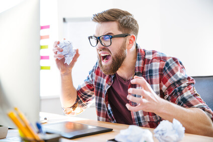 Angry crazy designer yelling and crumpling paper on his workplace